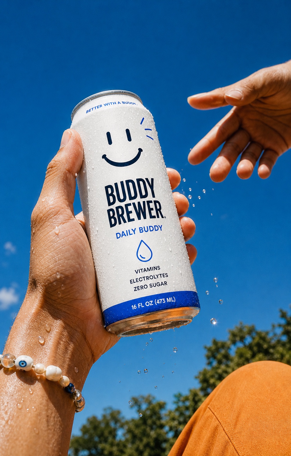 A hand passes a cold Daily Buddy can under a bright blue sky.